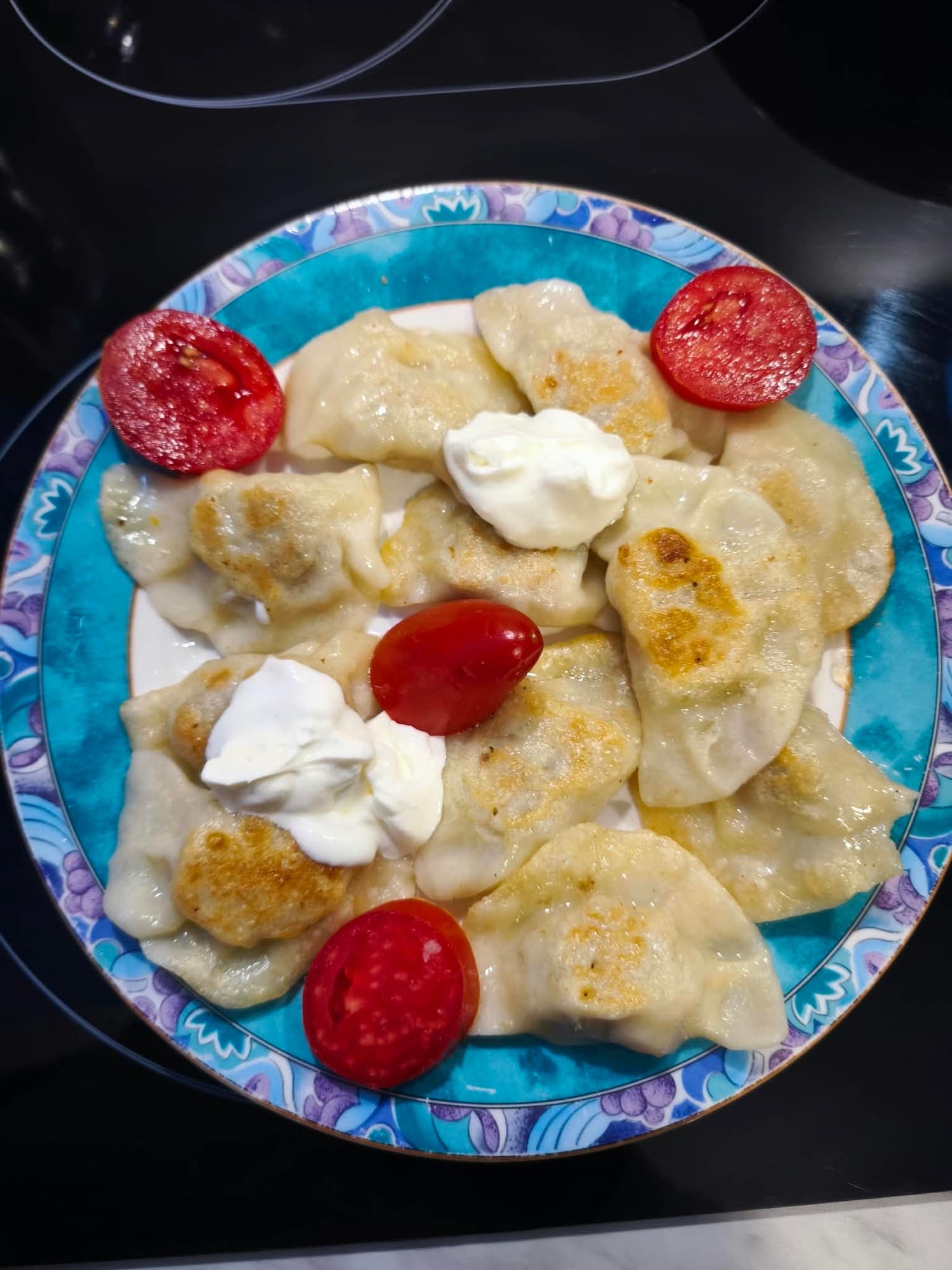 Pierogi ruskie mit saurer Sahne, auf dem Teller mit Tomaten